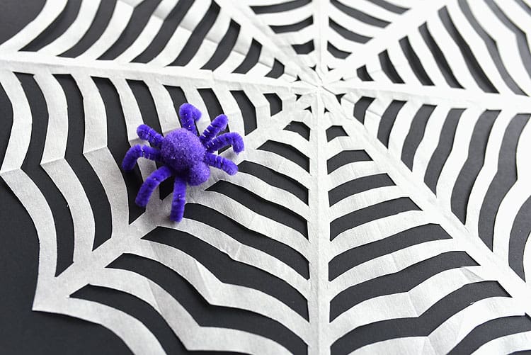 Closeup of a paper spiderweb with a pompom and pipe cleaner spider on it