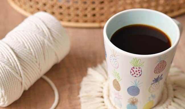 DIY Macrame Coasters Macrame coasters with cord and a coffee mug in the background