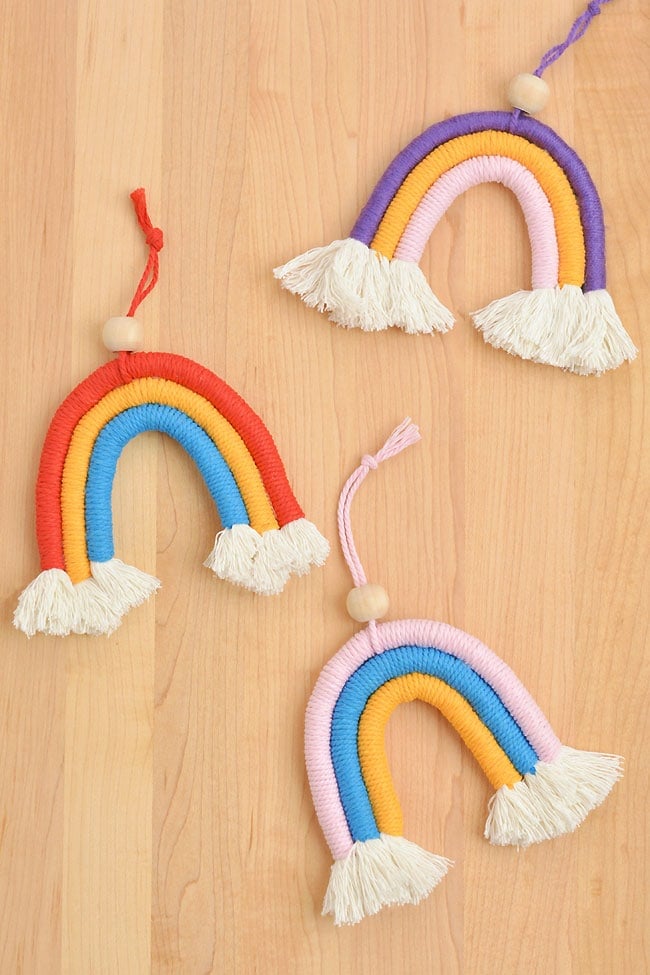 Three DIY macrame rainbows laid out on a wooden surface