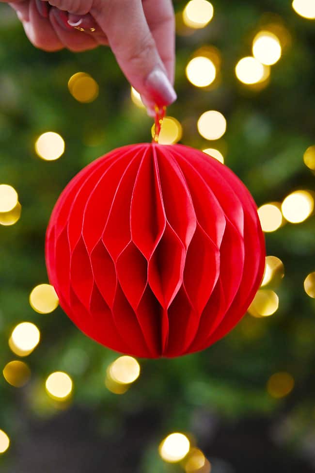 DIY paper honeycomb ornament in front of a Christmas tree