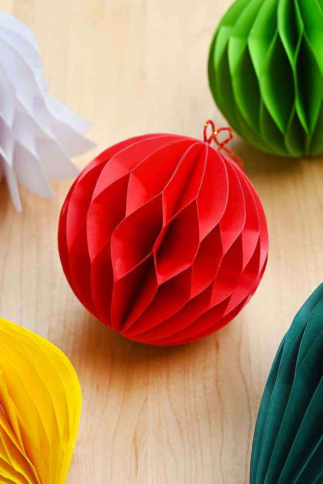 Red honeycomb ball ornament sitting with other DIY Christmas ornaments