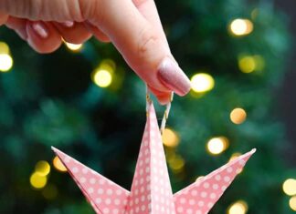 How to Make Paper Star Ornaments Holding a paper star ornament in front of a lit Christmas tree