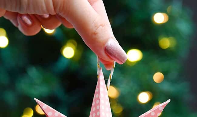 How to Make Paper Star Ornaments Holding a paper star ornament in front of a lit Christmas tree