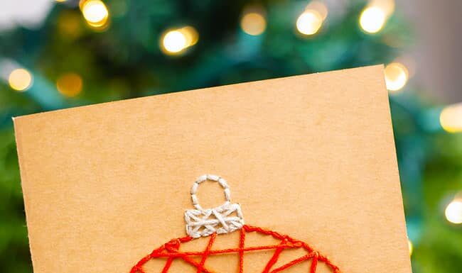 How to Make String Art Christmas Cards String art Christmas card held in front of a Christmas tree