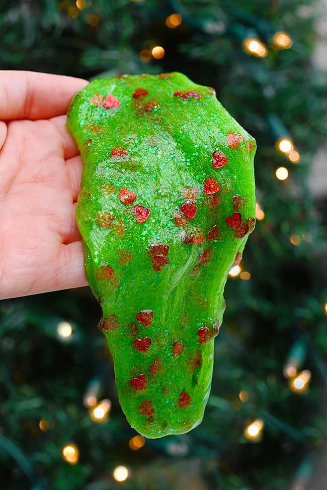 Grinch Slime Recipe with Jar Playing with Grinch slime in front of the Christmas tree