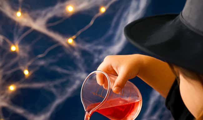 Fizzy Witch Cauldron – Fun Bubbling Brew Experiment for Kids Pouring colored vinegar into a baking soda filled witch cauldron